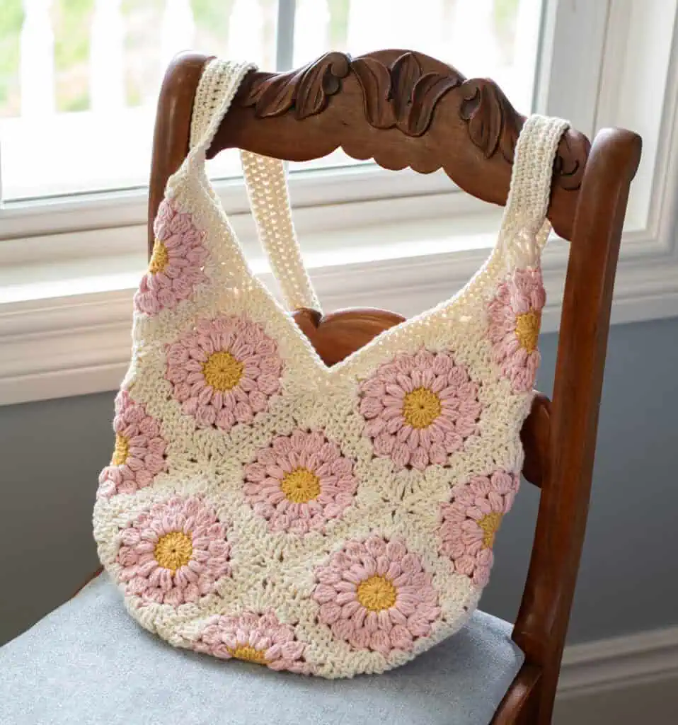 Pink and yellow flower granny square bag on blue chair next to window