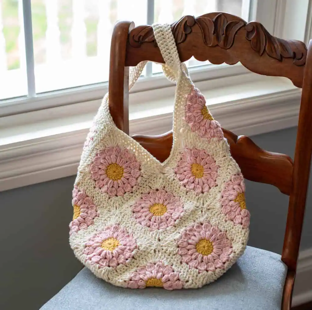 Pink and yellow flower granny square bag on blue chair next to window