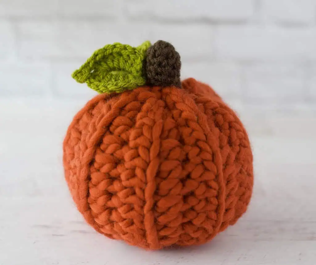 Orange crochet pumpkin with green leaves and dark brown stem